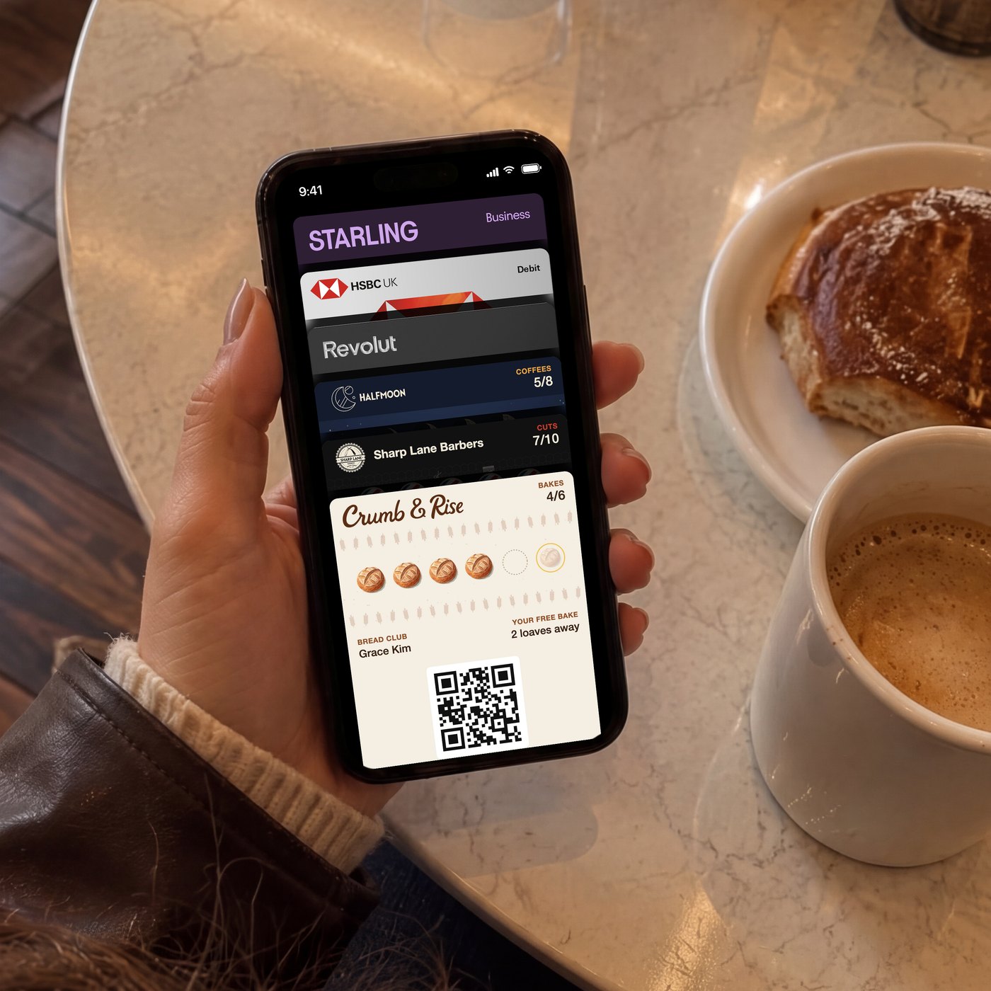 A customer in a cafe holding an iPhone with three loyalty cards in Apple Wallet